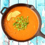Taco dip in skillet with green onions on top and tortilla chips dipped in.