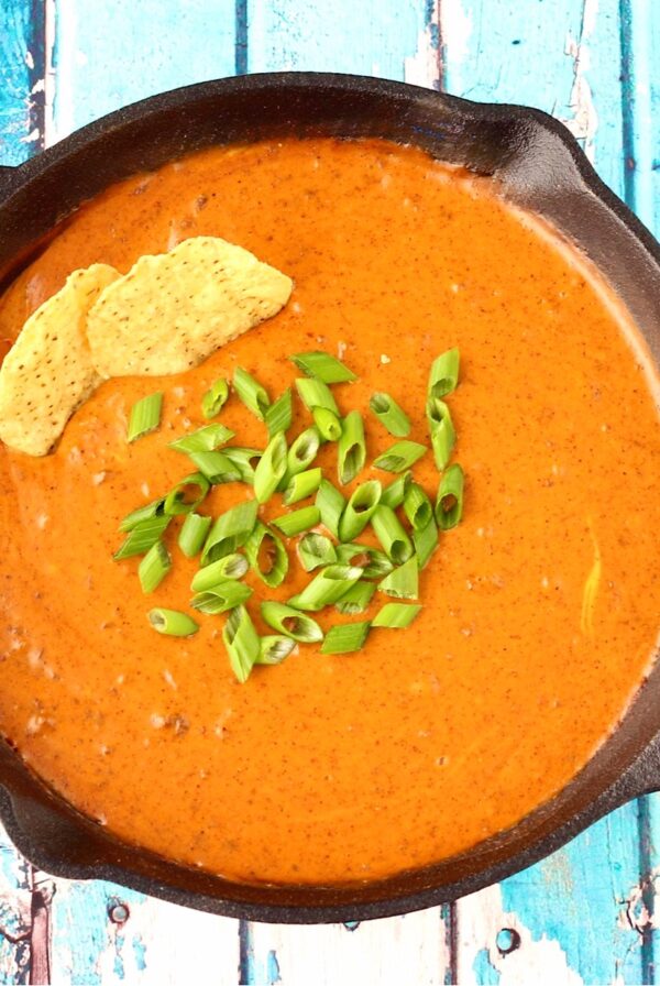 Taco dip in skillet with green onions on top and tortilla chips dipped in.
