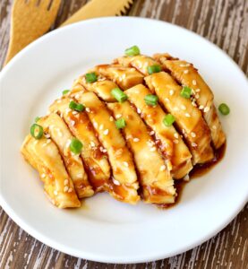 Sliced teriyaki chicken on plate garnished with green onions and sesame seeds.