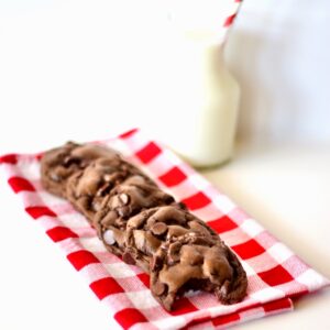 Triple chocolate cookies stacked on napkin with glass of milk in the background.