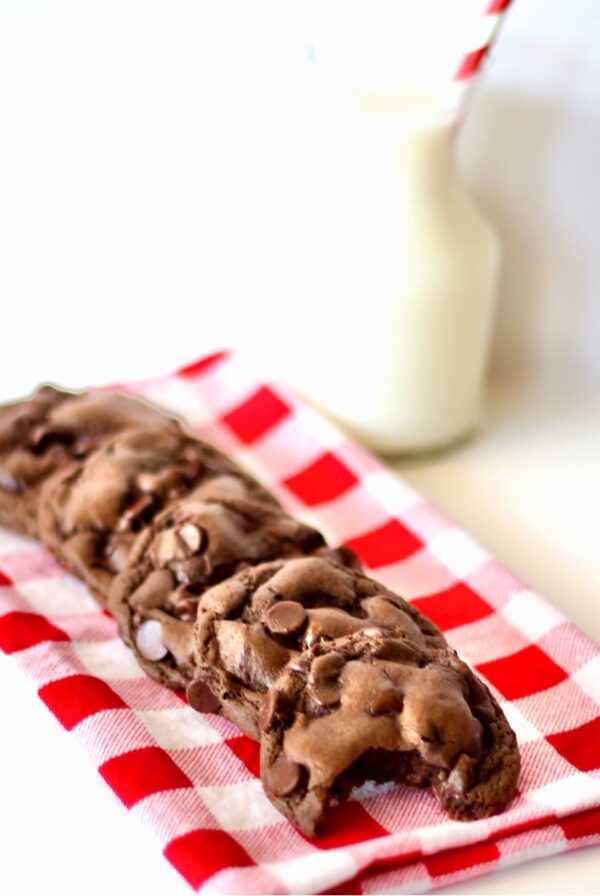 Triple chocolate cookies stacked on napkin with glass of milk in the background.