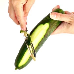 One hand holding cucumber while other hand peeling cucumber.
