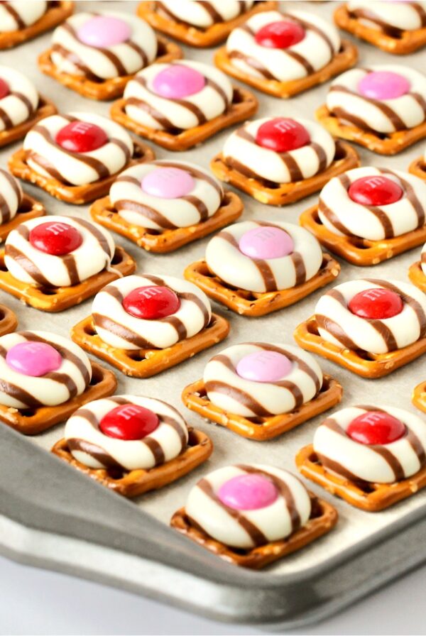Valentine pretzel treats with Hershey Hugs and spring M&M's on cookie sheet.