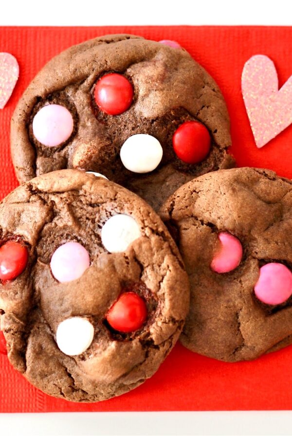 Three chocolate M&M Valentine's Day Cookies on napkin with hearts to the side.