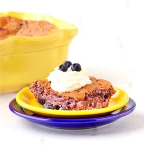 Piece of blueberry angel food cake on plate with whip cream and fresh blueberries on top.