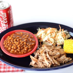 BBQ pulled pork on platter with coleslaw, corn on the cob, and barbecue baked beans to the side.
