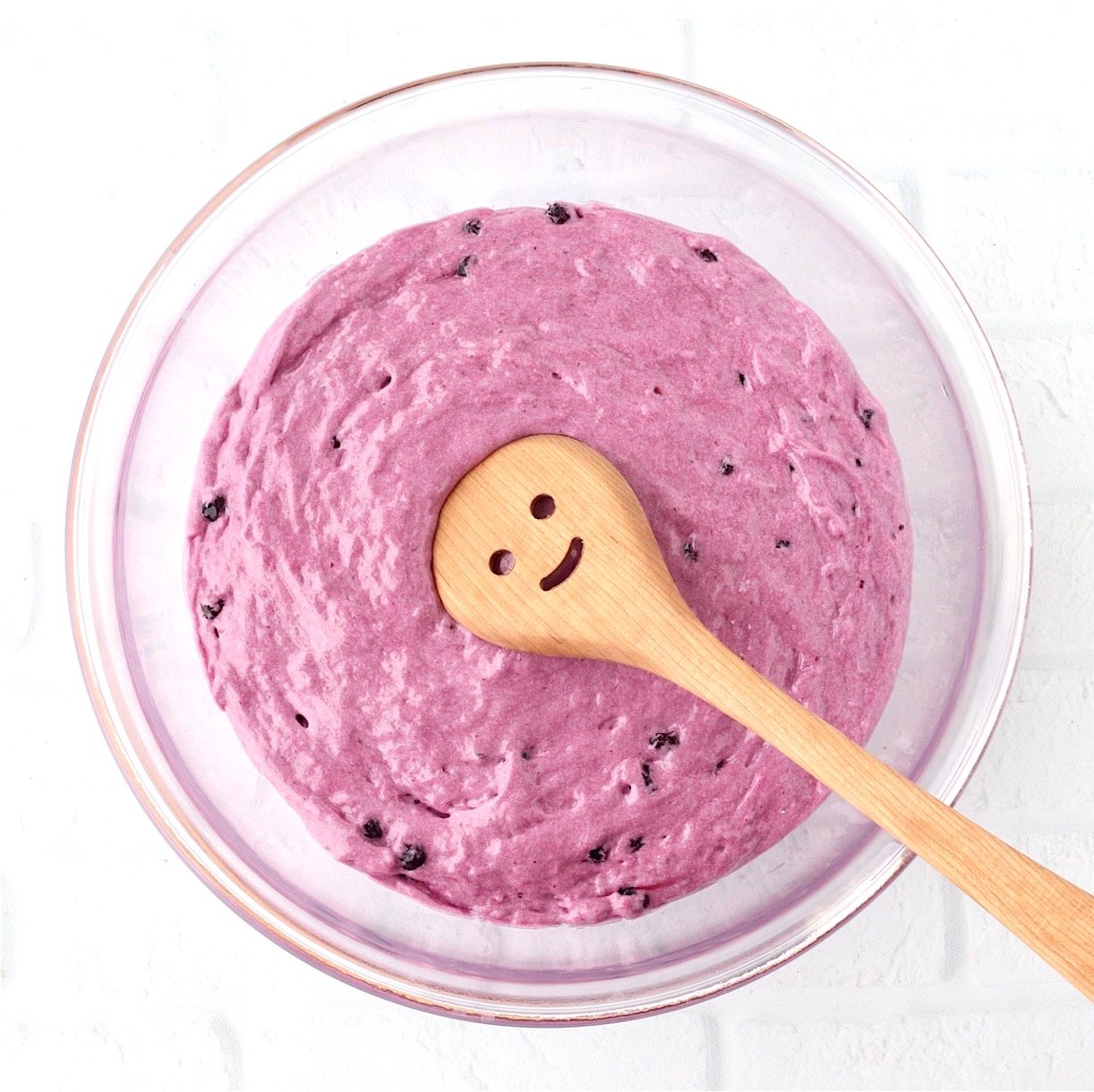 Blueberry angel food cake batter in bowl with wooden spoon.