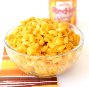 Buffalo Mac and cheese in bowl with wings hot sauce bottle in background.