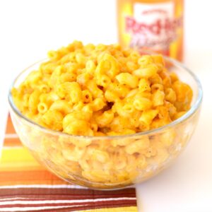 Buffalo Mac and cheese in bowl with wings hot sauce bottle in background.