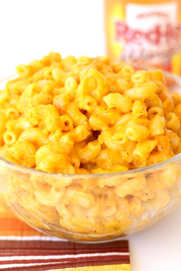 Buffalo Mac and cheese in bowl with wings hot sauce bottle in background.