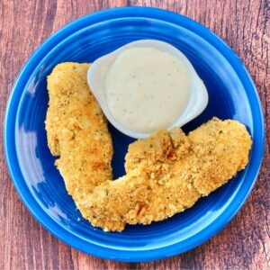 Two buttermilk chicken fingers on plate with ranch dipping sauce to the side.