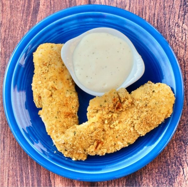 Two buttermilk chicken fingers on plate with ranch dipping sauce to the side.