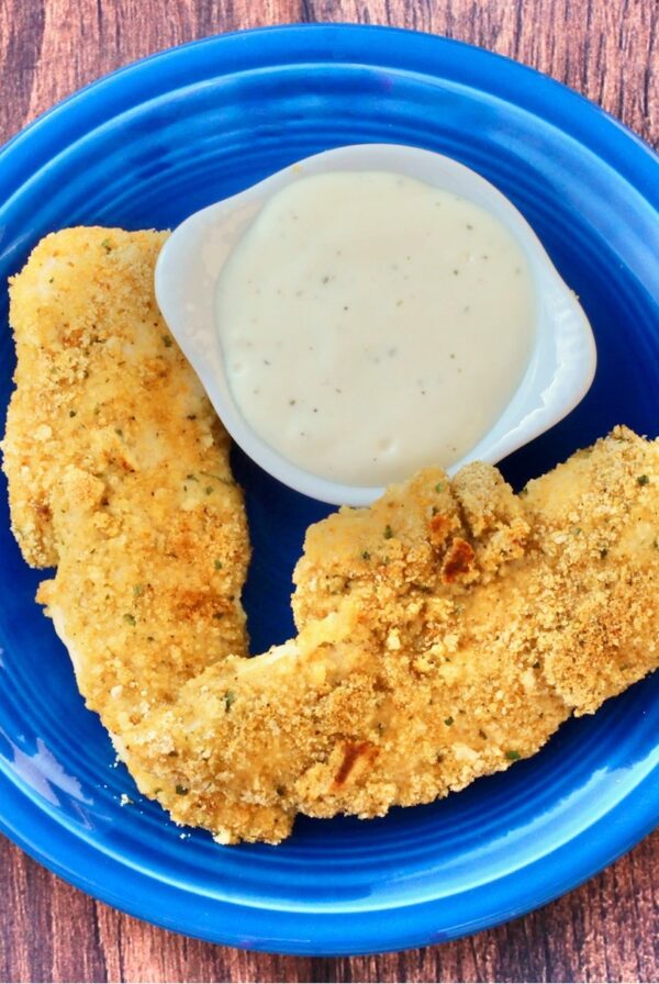 Two buttermilk chicken fingers on plate with ranch dipping sauce to the side.