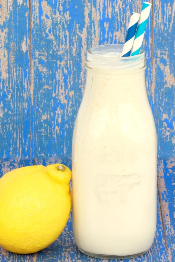 Frosted lemonade in milk jar with straws and a lemon to the side.