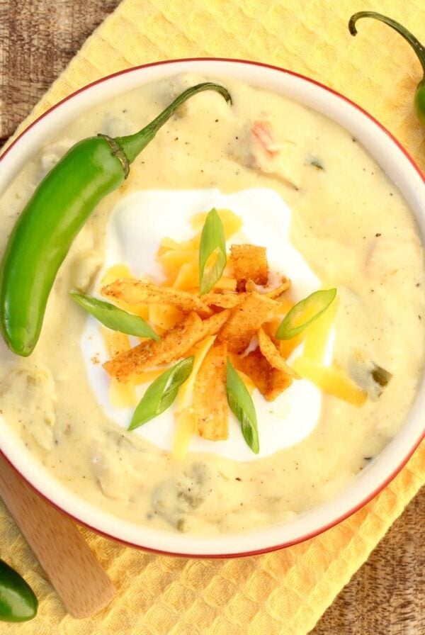 Creamy chicken enchilada soup in bowl with sour cream, shredded cheddar, tortilla strips and green onions on top.