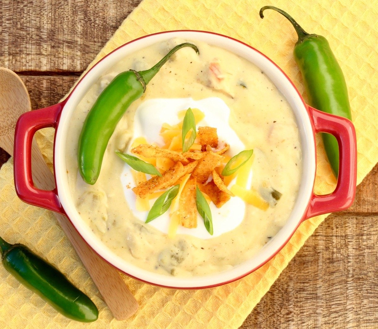 Creamy chicken enchilada soup in bowl with sour cream, shredded cheddar, tortilla strips and green onions on top.