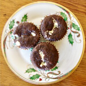 Three double chocolate chip cupcakes with cream cheese on plate.