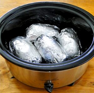 Four baked potatoes wrapped in foil in crock pot.