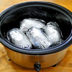 Four baked potatoes wrapped in foil in crock pot.