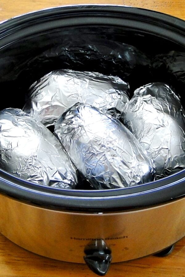 Four baked potatoes wrapped in foil in crock pot.