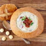 Clam chowder in bread bowl, garnished with bacon and parsley.