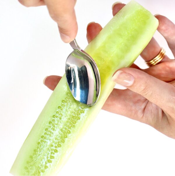 Hands holding peeled cucumber while spoon is removing seeds.