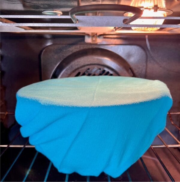 Dough proofing in covered bowl inside oven under light.