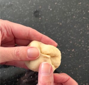 Hands shaping dough ball by stretching and folding.