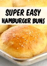 Homemade hamburger buns topped with sesame seeds on baking sheet.
