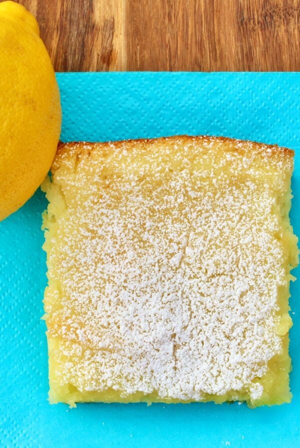 Lemon bar square on napkin with lemon to the side.