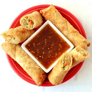 Egg rolls on plate surrounding small dish with egg roll dipping sauce.