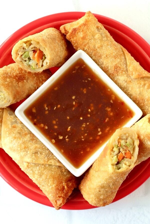 Egg rolls on plate surrounding small dish with egg roll dipping sauce.