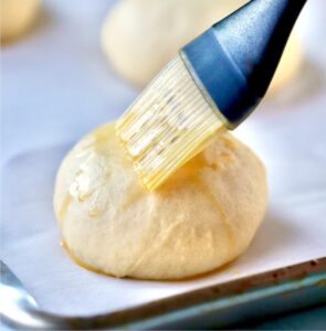 Egg wash being brushed on mini slider buns before baking.