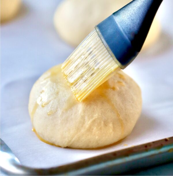 Egg wash being brushed on mini slider buns before baking.