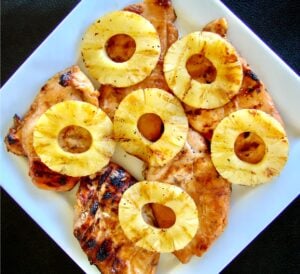 Five pieces of grilled teriyaki chicken on plate topped with grilled pineapple rings.