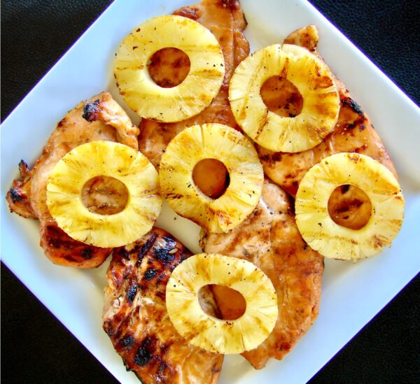 Five pieces of grilled teriyaki chicken on plate topped with grilled pineapple rings.