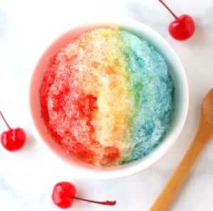Shaved ice snow cone in bowl with rainbow colors of snow cone syrup.