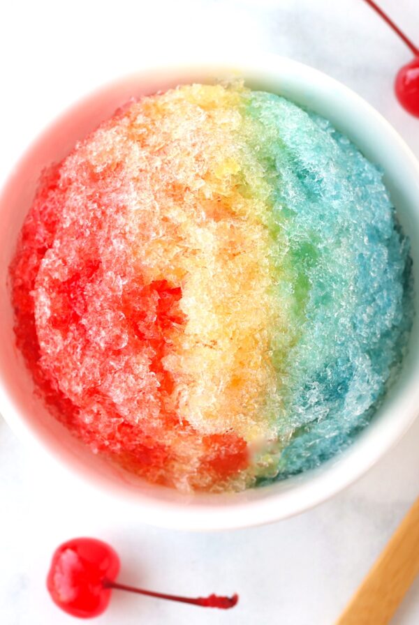 Shaved ice snow cone in bowl with rainbow colors of snow cone syrup.
