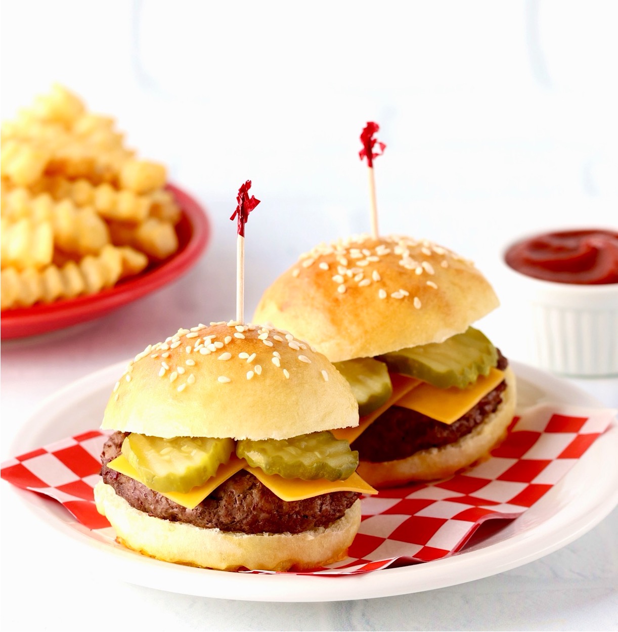 Two mini slider buns with mini burgers, cheese and pickles.