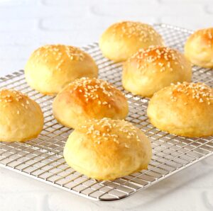 Baked homemade slider buns topped with sesame seeds on cooling rack.