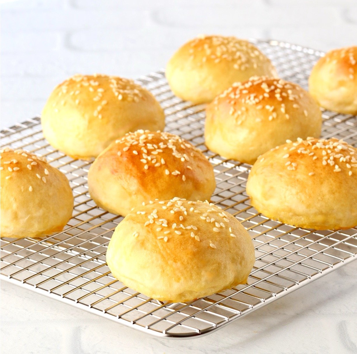 Baked homemade slider buns topped with sesame seeds on cooling rack.