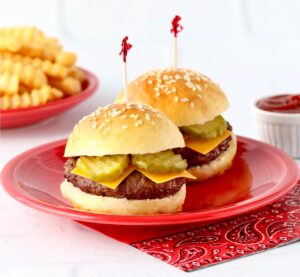 Two slider buns with burger patties, cheese and pickles inside, and French fries and ketchup to the side.