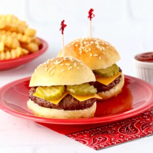 Two slider buns with burger patties, cheese and pickles inside, and French fries and ketchup to the side.