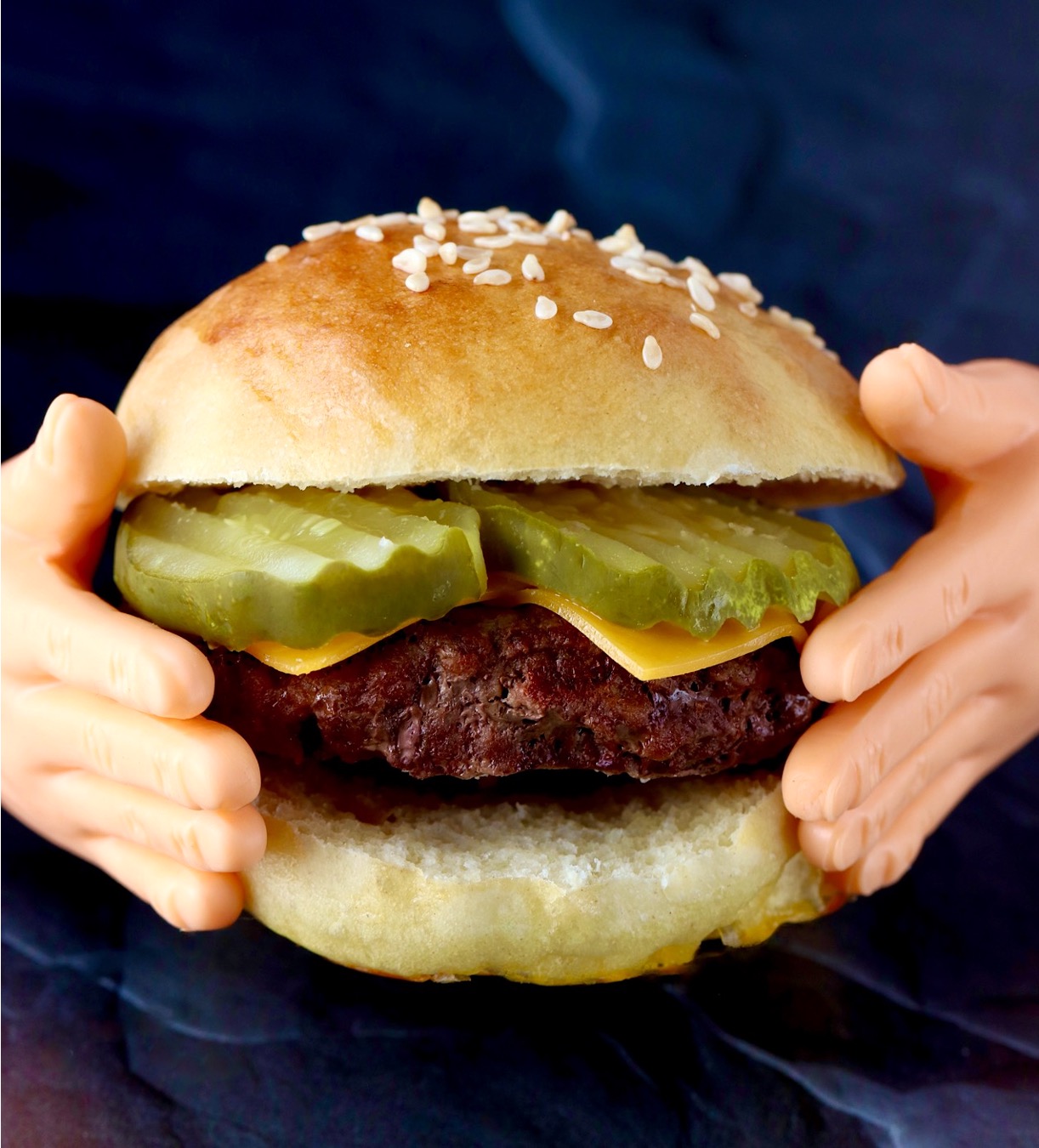 Tiny hands holding small burger with cheese and pickles on mini slider bun.