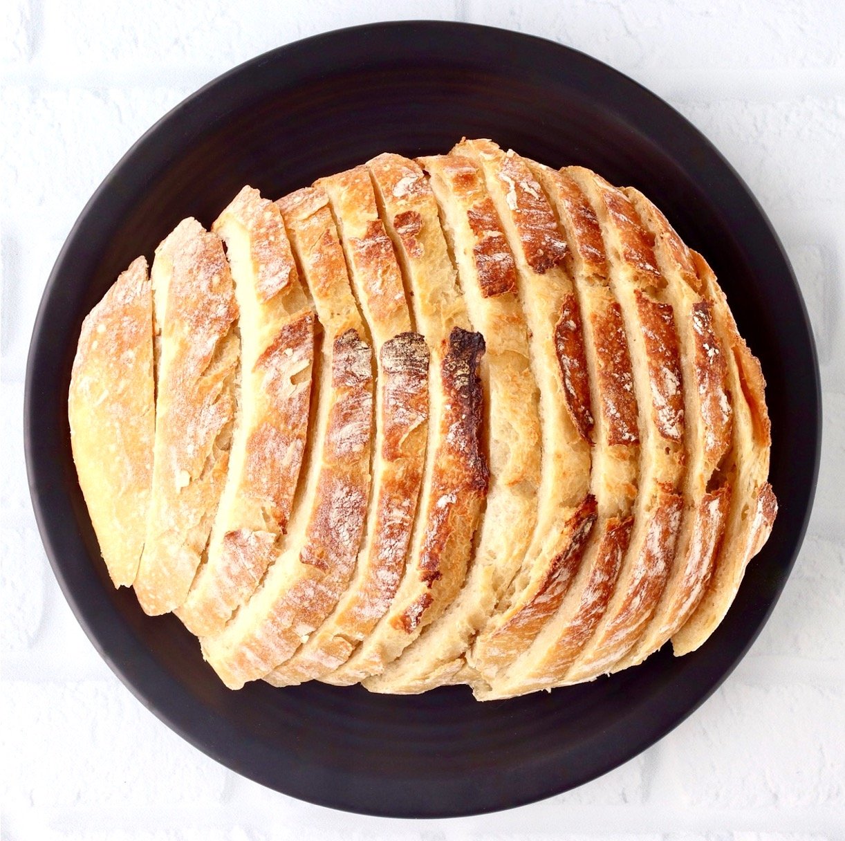 Sliced sourdough bread loaf on black plate.
