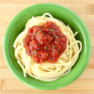 Spaghetti sauce on top of spaghetti noodles in green dish.