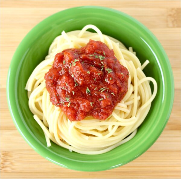 Spaghetti sauce on top of spaghetti noodles in green dish.