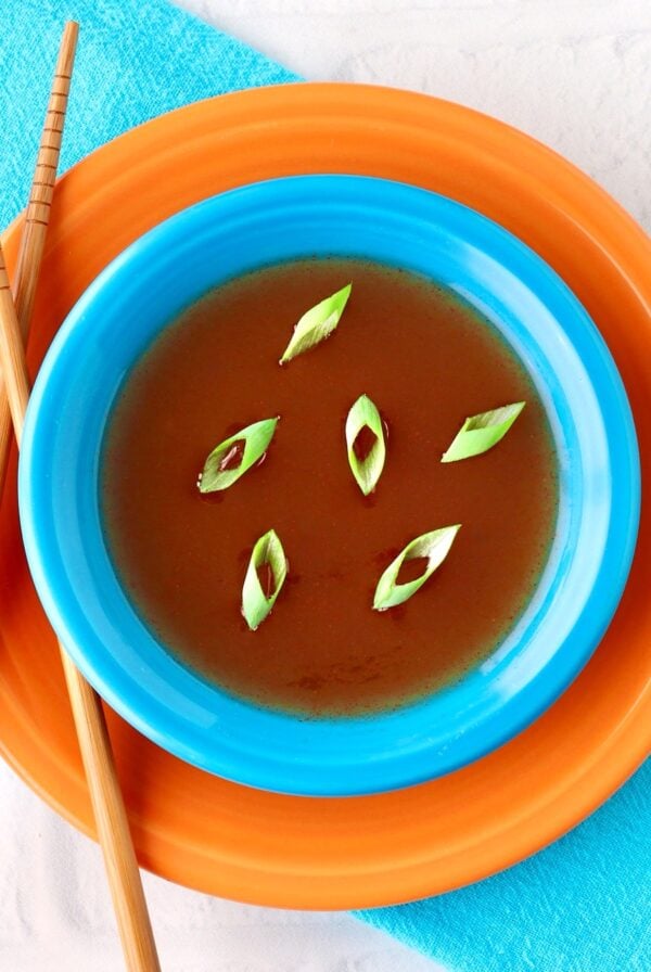 Sweet and Sour sauce in dish garnished with green onions and chopsticks to the side.