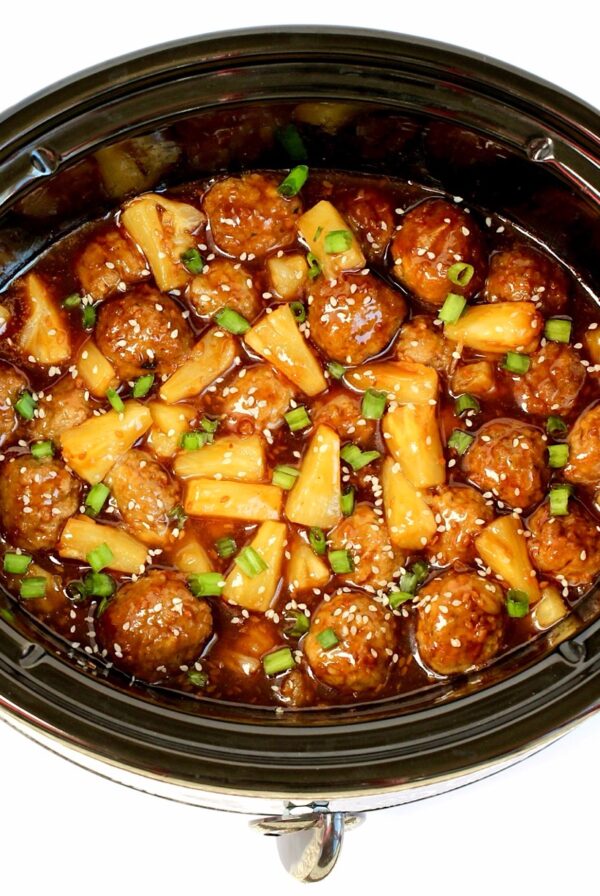 Teriyaki meatballs with pineapple, green onions, and sesame seeds in crock pot.