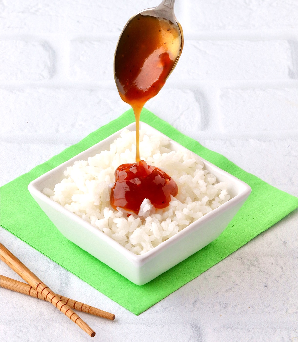 Teriyaki pineapple sauce being drizzled onto white sticky rice from spoon.
